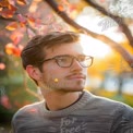 Thoughtful Young Man in Autumn Park with Colorful Leaves and Soft Sunset Light