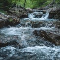 Tranquil Mountain Stream: Serene Waterfall Flowing Through Lush Greenery