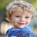 Adorable Smiling Toddler with Curly Hair and Bright Blue Eyes in Natural Outdoor Setting