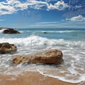 Tranquil Beach Scene with Waves and Rocky Shoreline Under Blue Sky